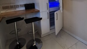 A compact kitchen with white cabinets, a wooden countertop, two black bar stools, and a built-in oven. - Umbrella Properties Woolwich London  (London)
