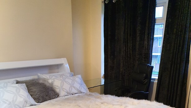 A bedroom with a large bed, a wooden floor, and a window with curtains. - Umbrella Properties Woolwich London  (London)