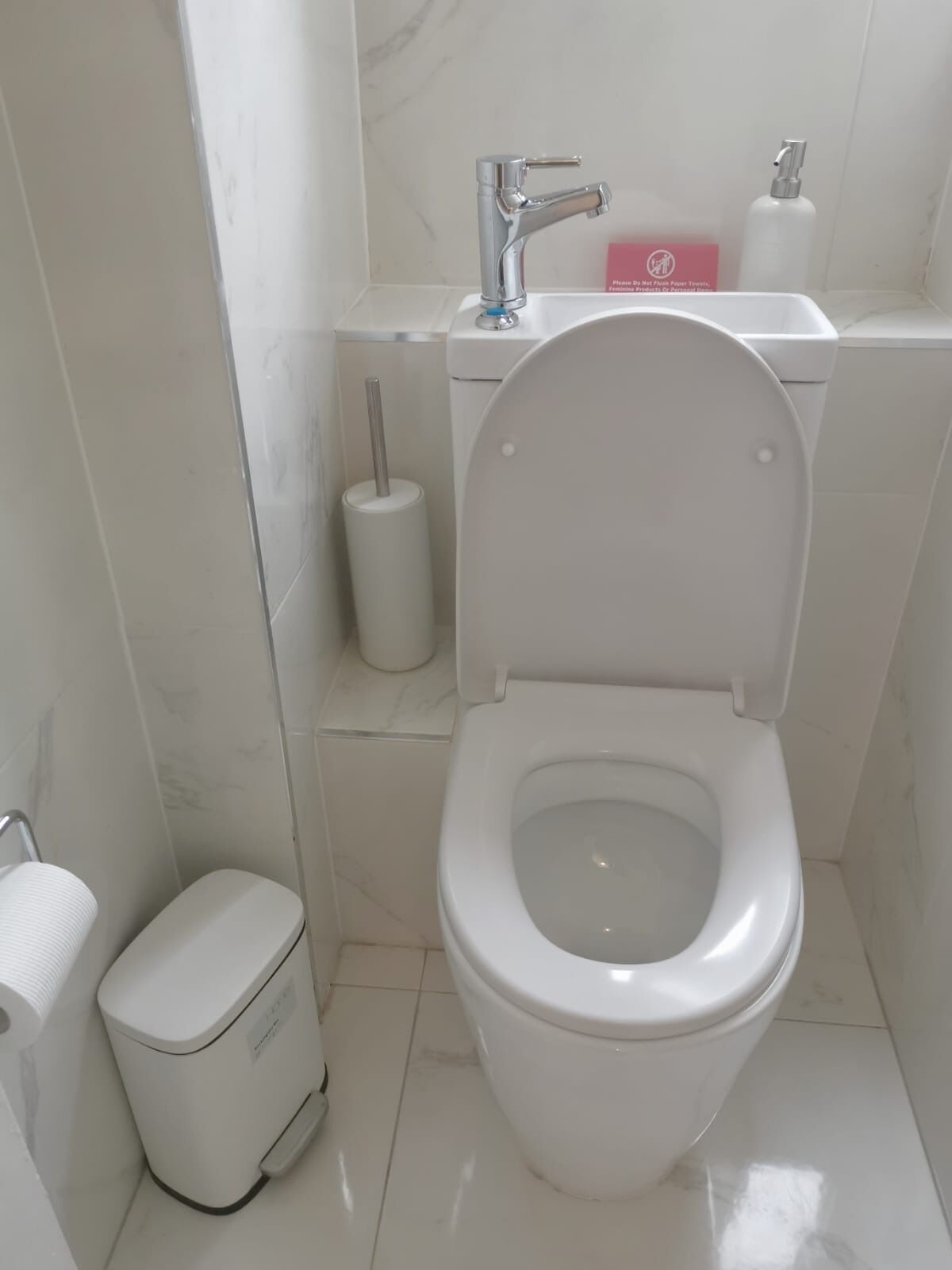 A modern bathroom with a white toilet, a hand dryer, a trash bin, and a sink with a faucet.
