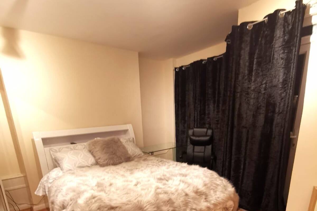 A bedroom with a large bed, a chair, and a window with black curtains.