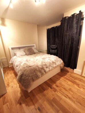 A bedroom with a large bed, a chair, and a window with black curtains. - Umbrella Properties Woolwich London (London)