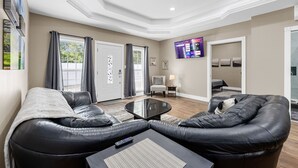A modern living room with leather sofas, a glass coffee table, and a flat-screen TV mounted on the wall.