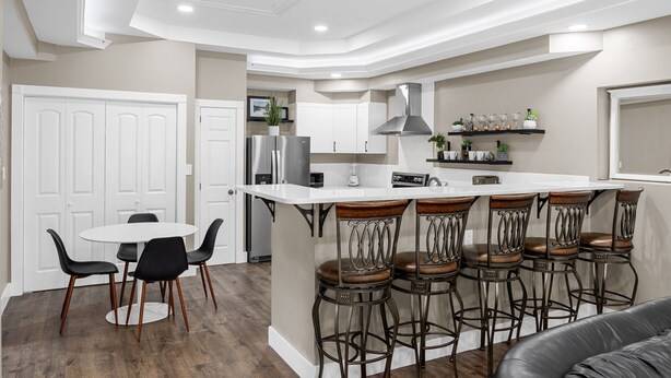 A modern kitchen with a central island, bar stools, and a dining area with chairs.