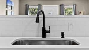 A modern kitchen with a stainless steel sink, black faucet, and white tiled backsplash.