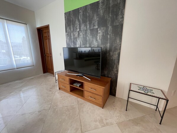 A room with a wooden TV stand, a flat-screen TV, a small table, and a patterned table runner.