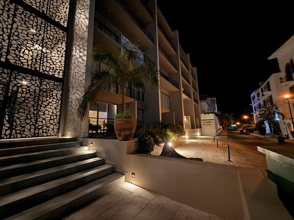 A multi-story hotel with a modern facade, outdoor lighting, and a staircase leading to the entrance.
