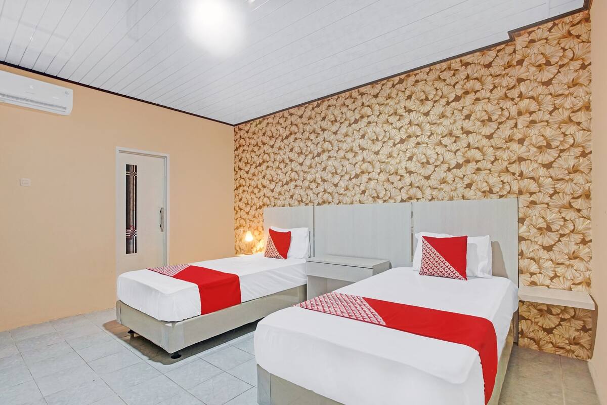 A hotel room with two beds, each with white bedding and red accents, a wooden textured wall, and a ceiling with a grid pattern.