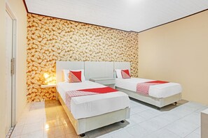 A hotel room with two beds, a white headboard, a wall with a shell pattern, and a small bedside table with a lamp.