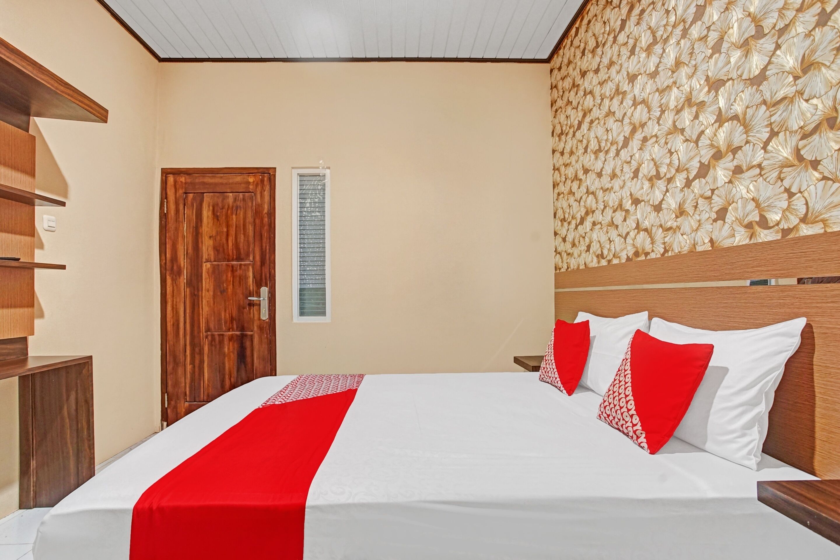Ein Hotelzimmer mit einem hölzernen Bett, einer roten und weißen Bettdecke, einem Holz-Kopfteil und einer dekorativen Wandverkleidung.