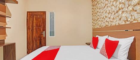 A hotel room with a wooden bed, a red and white bedspread, a wooden headboard, and a decorative wall panel.