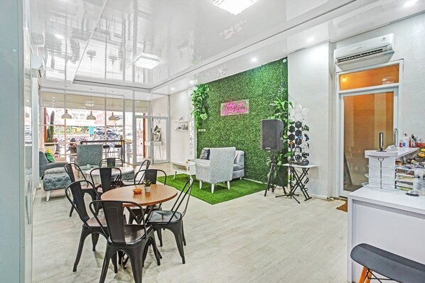 A modern indoor space with a dining area, a green wall with a neon sign, and a reception desk. - OYO 90399 Box House (Bandar Lampung)
