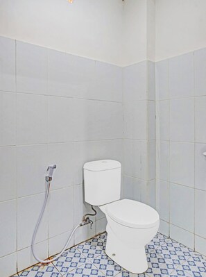 A small, white-tiled bathroom with a toilet and a visible water pipe.