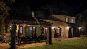 Una casa de piedra con un porche cubierto, mobiliario exterior y un pilar de piedra.