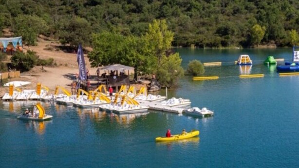 Un lago con barcos, un muelle y una colina boscosa al fondo.