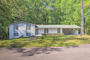 A two-story white house with a green roof, surrounded by trees.