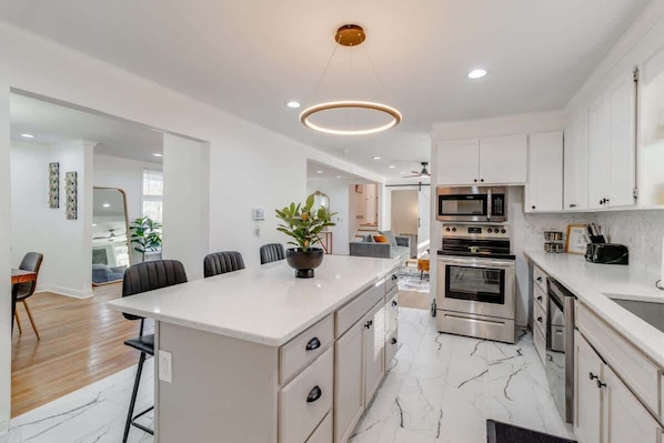 A modern kitchen with white cabinetry, a central island, stainless steel appliances, and a marble floor.