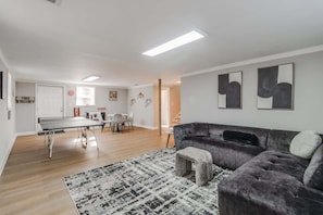 A modern living room with a grey sofa, a small ottoman, a ping pong table, and a patterned rug.