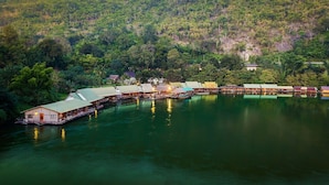 A series of overwater bungalows connected by walkways over a calm lake, surrounded by dense forest. - River Kwai Jungle View (Sai Yok)