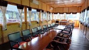 A conference room with a long wooden table and chairs, large windows with curtains, and an air conditioning unit on the wall. - River Kwai Jungle View (Sai Yok)