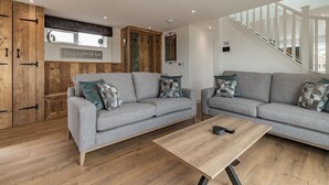 A modern living room with two grey sofas, wooden flooring, a wooden cabinet, and a staircase. - 3 bedroom accommodation in Church Broughton, near Derby (Church Broughton, near Derby)