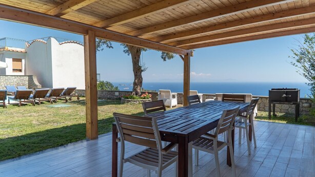 An outdoor patio with a wooden table and chairs, a barbecue grill, and a view of the sea. - Apartment Luna with Pool (Nerano)