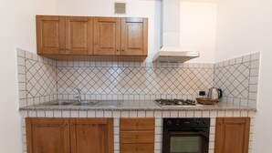 A compact kitchen with wooden cabinets, a gas stove, a built-in oven, and a sink. - Apartment Luna with Pool (Nerano)