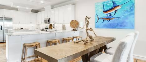 Une cuisine moderne avec des meubles blancs, un îlot central en bois et un coin repas comprenant une table en bois et des chaises blanches.