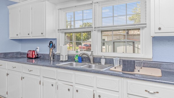 A kitchen with white cabinets, a double sink, and a window with blinds. - ReNew At JW's & bring your Dog too! (Florence)