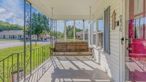 A covered porch with a wooden bench, a metal railing, and a clear view of the street and houses in the background. - ReNew At JW's & bring your Dog too! (Florence)
