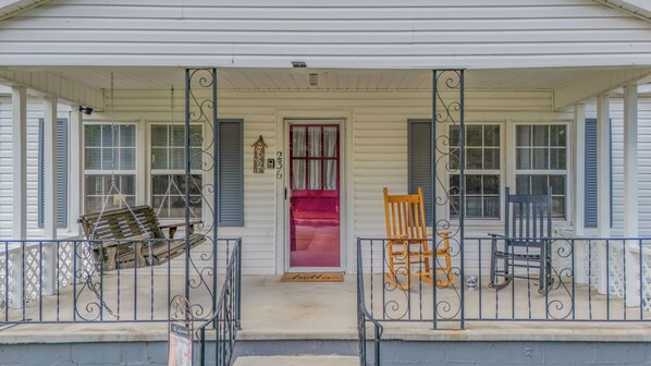 A porch with a red door, two rocking chairs, and a 'welcome' mat.