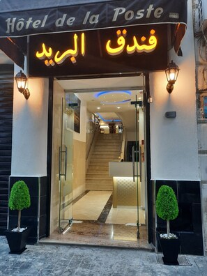 The entrance of Hotel de la Poste with a modern design, featuring a glass door, a staircase, and potted plants. - Hotel de la Poste (Algiers)