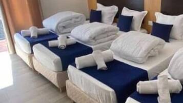Une chambre d’hôtel avec plusieurs lits, chacun étant équipé de draps blancs et d’une couvre-lit bleue.