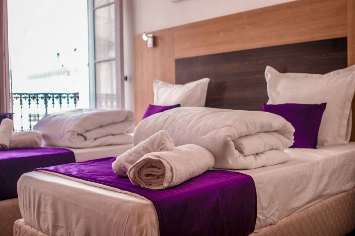 A hotel room with two beds, each with white linens and purple accents.