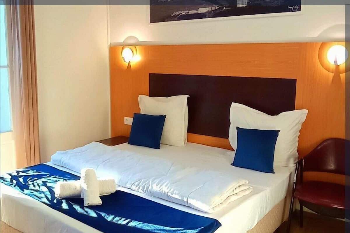 A hotel room with a large bed, two bedside lamps, a chair, and a view of the city.