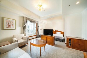 A well-lit hotel room with a sofa, a round wooden coffee table, a TV on a wooden cabinet, and a bed with a white comforter. - Koko Hotel Osaka Shinsaibashi (Osaka)