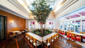 Un amplio comedor interior con un árbol central, suelo de madera y múltiples mesas y sillas.