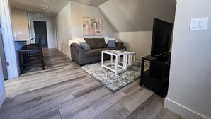 A living room with a sofa, a coffee table, and a TV. There is a dining area with a table and chairs. The room has wooden flooring and a ceiling light. - S Broadway 2 bed getaway w Parking - 98 walk score (Denver)