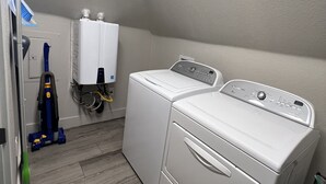A laundry room with a front-loading washer and dryer, a vacuum cleaner, and a water heater. - S Broadway 2 bed getaway w Parking - 98 walk score (Denver)