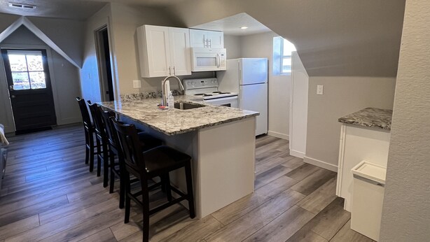 A modern kitchen with a central island, white cabinets, and a wood floor. - S Broadway 2 bed getaway w Parking - 98 walk score (Denver)