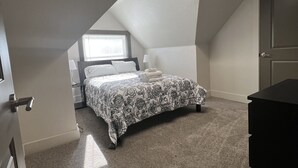 A bedroom with a sloped ceiling, a bed with a floral bedspread, a nightstand, a dresser, and a window with blinds. - S Broadway 2 bed getaway w Parking - 98 walk score (Denver)