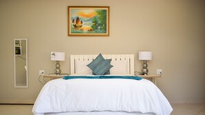 A hotel room with a large bed, a painting of a landscape above it, a mirror on the left, and two bedside lamps. - Protea Guesthouse  (Newcastle)