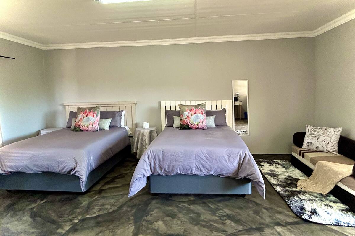 A bedroom with two beds, a bedside table, a chair, a mirror, and a patterned rug.
