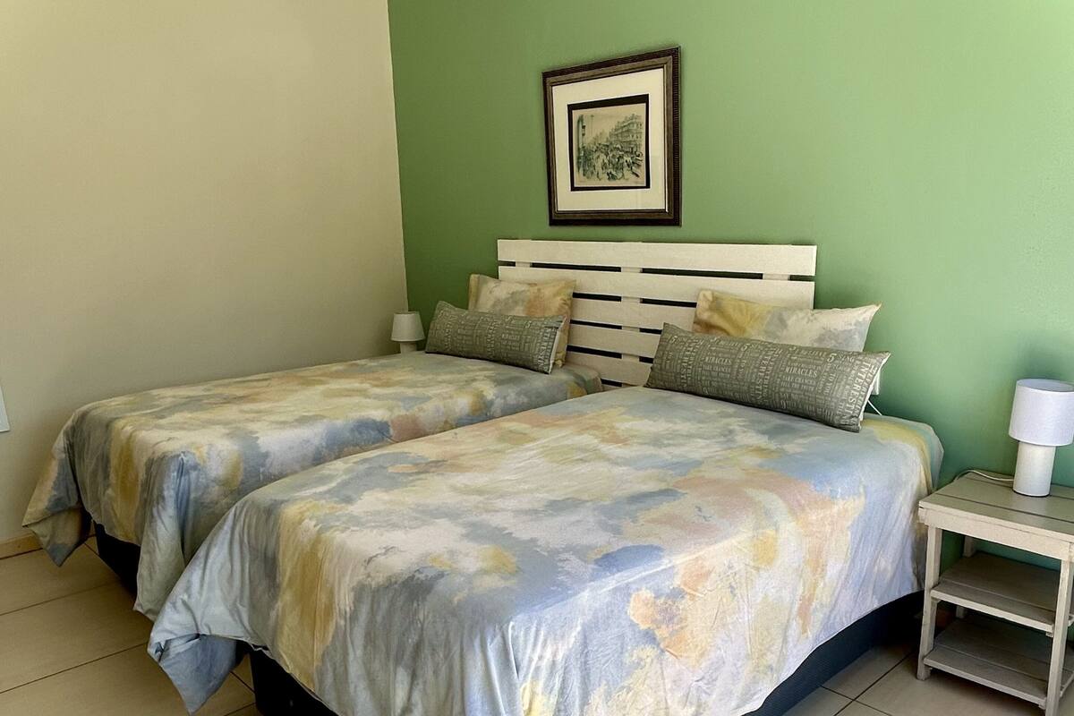 A bedroom with two beds, a nightstand, a framed picture on the wall, and a tiled floor.