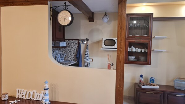 A kitchen with a clock, a microwave, and a cabinet with dishes. - Vacation House La dimora nel borgo (Taranto)