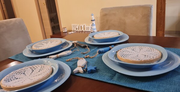 A dining table with four blue plates, each with a white lace-patterned cake. A blue placemat covers the table, and a small lighthouse decoration is visible in the background. - Vacation House La dimora nel borgo (Taranto)