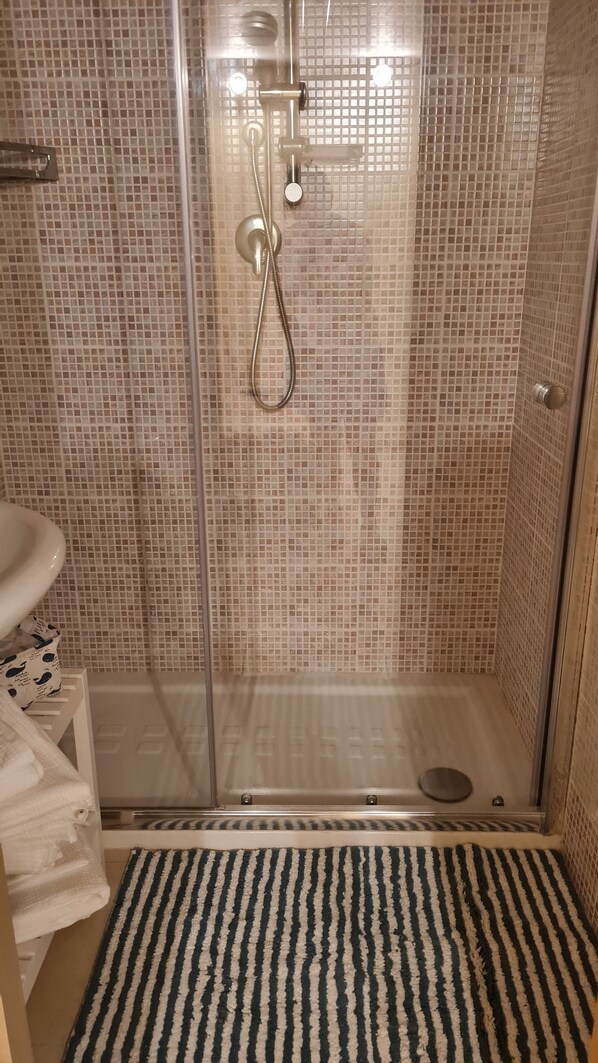 A shower with a glass door, a sink, and a striped rug.