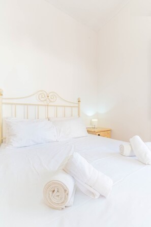 Un lit bien fait, avec du linge de lit blanc et des serviettes pliées, une tête de lit en bois et une table de chevet avec une lampe.
