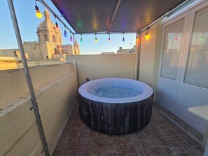 A hot tub on a rooftop terrace with a view of a historic building. - Townhouse with roof BBQ area & views (Iż-Żebbuġ)