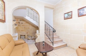 Un salon doté d’une cheminée en pierre, d’un escalier avec une rampe en fer forgé et de deux tableaux encadrés accrochés au mur.