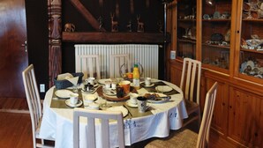 A dining table set with various dishes, cups, and a bottle, surrounded by chairs in a room with wooden walls and a cabinet with glass doors. - Your Nomadic Room: Africa (MARTHOD)